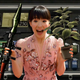 Marie Kondo holds up a rocket launcher and a green herb excitedly in front of Resident Evil 4's attaché case.